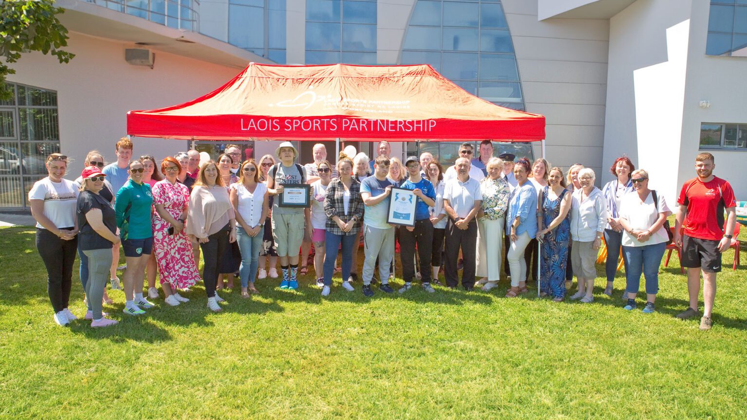 Group of people gather in garden underneath a red gazebo with Laois Sports Partnership logo on it.