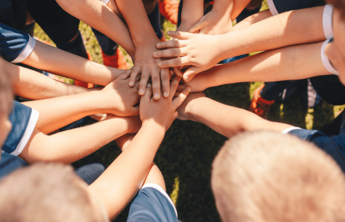 Children hold hands on top of one another in a circle.