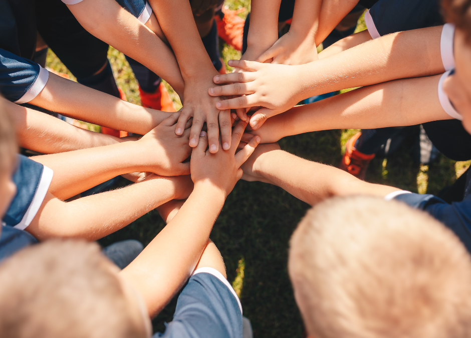 Children hold hands on top of one another in a circle.