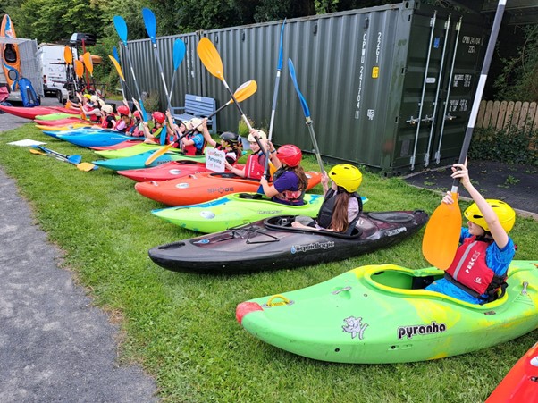 Group of young girls sit in kayaks on the grass and learn how to paddle.