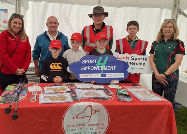 Children and adults stand behind table and hold sign for Sport 4 Empowerment.