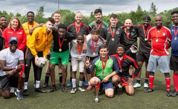 Group of athletes with medals around necks stand on pitch.