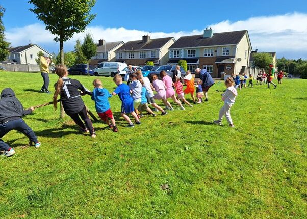 Children play tug of war on grass on a sunny day.