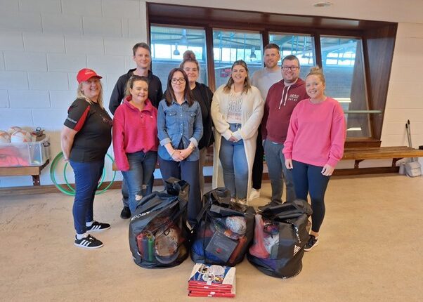 Group smile for picture behind three bags of sporting equipment.